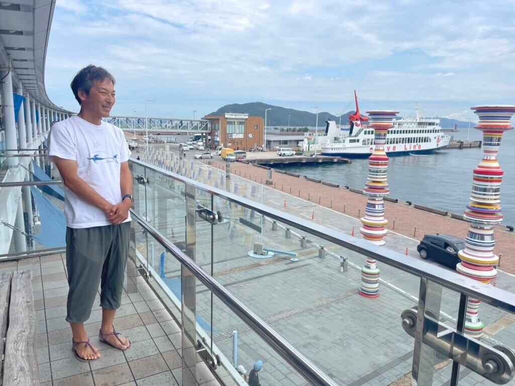 高松港から島々へのフェリーを眺める森田さん。足元には手作りワラーチ